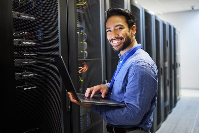 Man working on a laptop in a server room and smiling